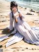 A woman in a long white dress sitting on a beach.