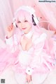 A woman in a pink dress and headphones sitting on a bed.