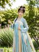 A woman in a blue and beige hanbok standing in a garden.