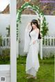 A woman in a white dress standing in front of a white fence.