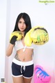 A woman in a white top and black shorts holding yellow boxing gloves.